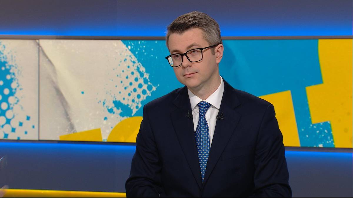 Mężczyzna w okularach i garniturze patrzy w bok.