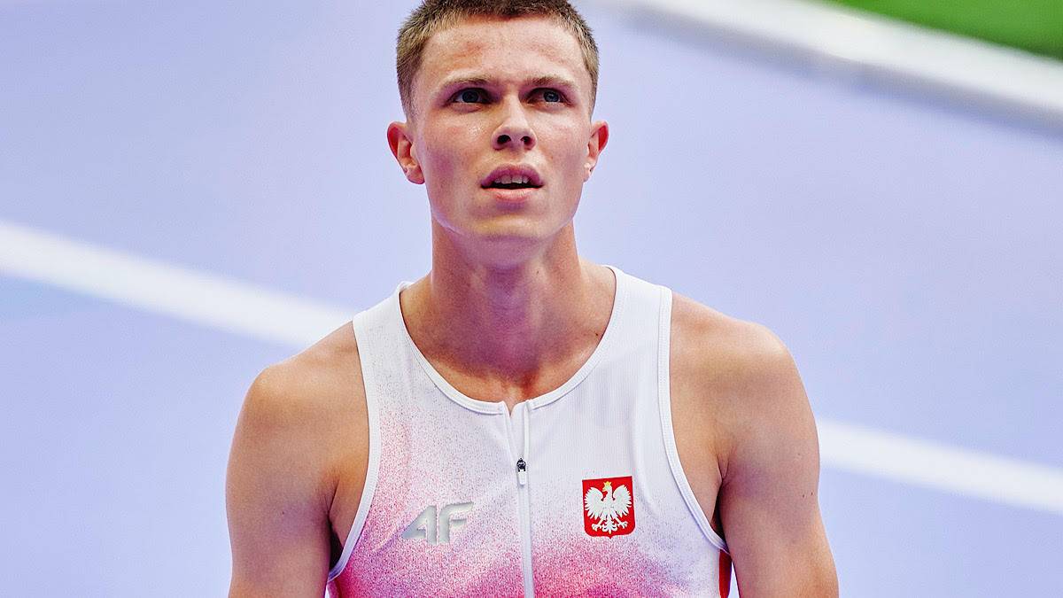 Mateusz Wyderka w stroju sportowym z godłem Polski, patrzący w bok podczas zawodów lekkoatletycznych.