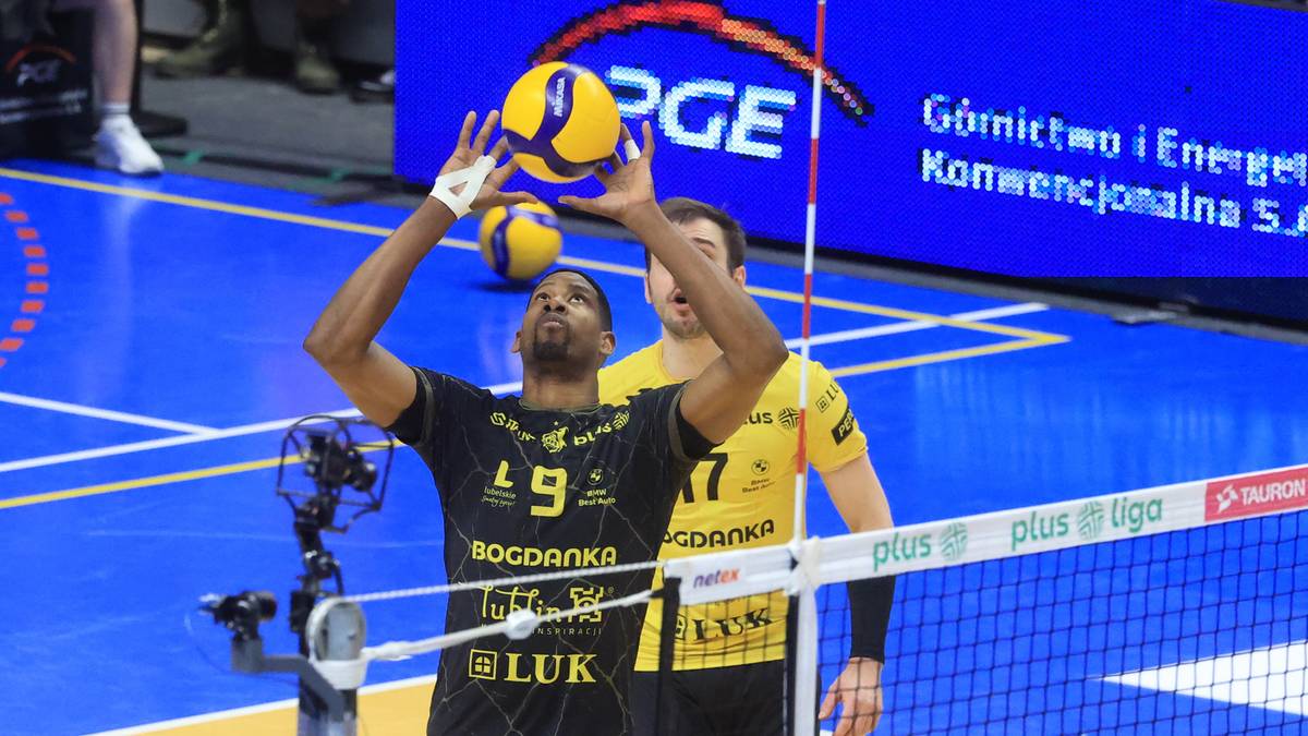 Siatkarz w czarnej koszulce z numerem 9 przygotowuje się do zagrywki, trzymając piłkę nad głową.