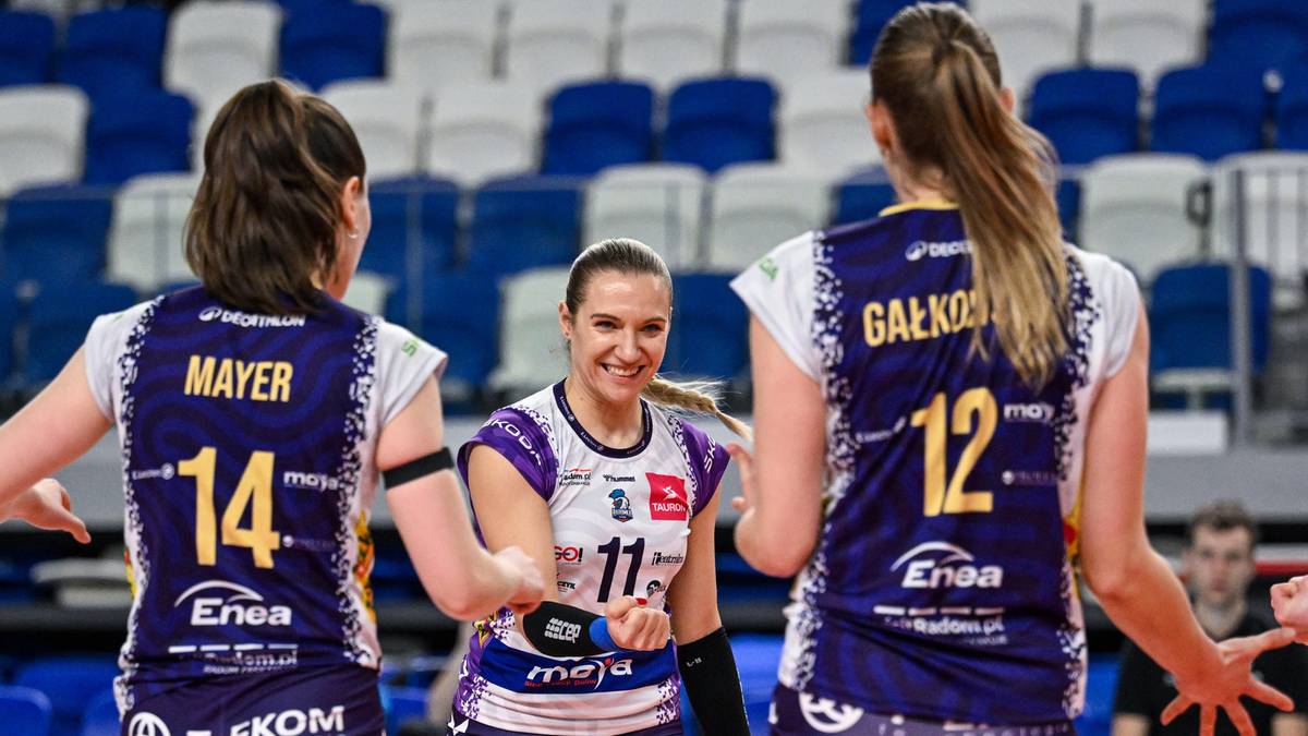 Trzy siatkarki w strojach sportowych stoją blisko siebie na boisku. Dwie z nich są odwrócone tyłem do widza, prezentując swoje numery na plecach. Jedna z nich, po lewej, ma numer 14 i nazwisko "MAYER". Druga, po prawej, ma numer 12 i nazwisko "GAŁKO". Środkowa siatkarka, zwrócona do widza, uśmiecha się i ma numer 11 na koszulce.