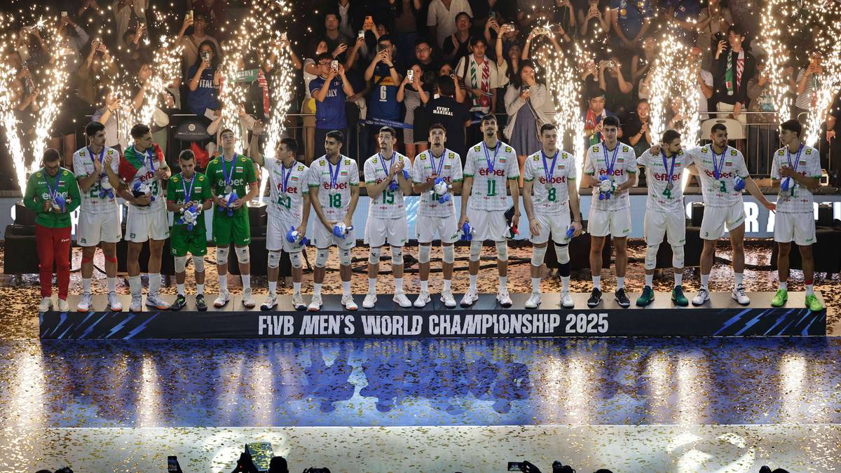 Reprezentacja Polski w piłce siatkowej w strojach sportowych stoi na podium podczas ceremonii wręczenia nagród za Mistrzostwa Świata. W tle widownia i efekty pirotechniczne.