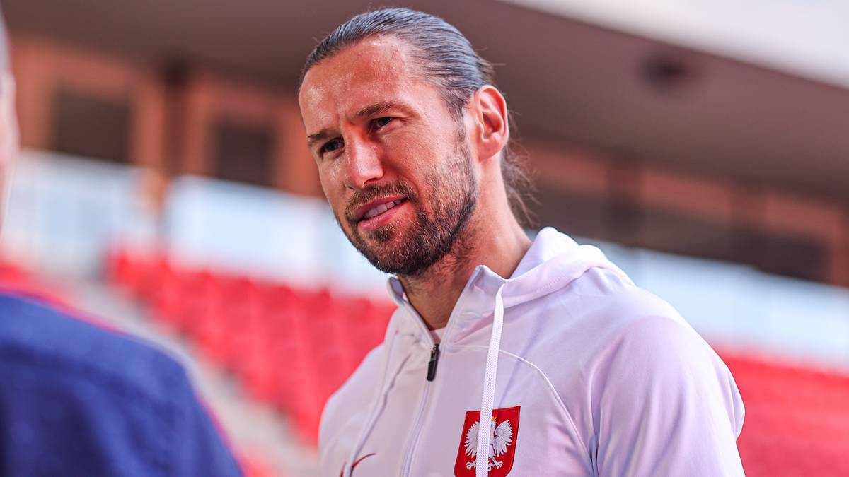 Grzegorz Krychowiak, polski piłkarz, w białej bluzie z kapturem z godłem Polski, z włosami związanymi w kucyk.