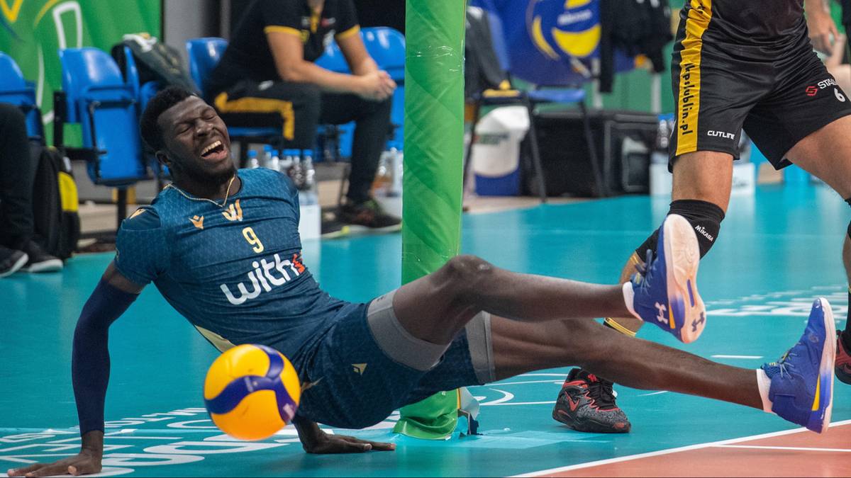 Siatkarz w niebieskim stroju leży na parkiecie, pr&oacute;bując odbić piłkę podczas meczu.