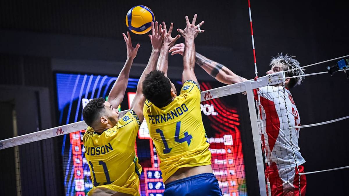 Trzech siatkarzy walczących o piłkę nad siatką podczas meczu.