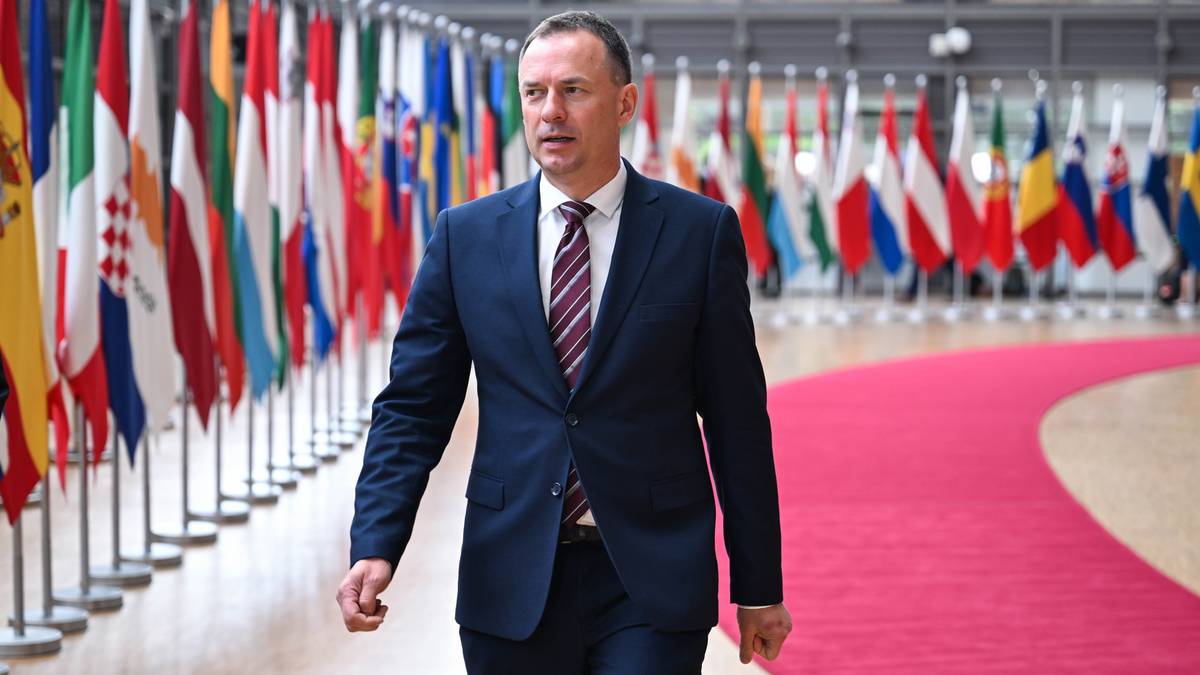 Mężczyzna w garniturze idzie po czerwonym dywanie, na tle rzędu flag państwowych.