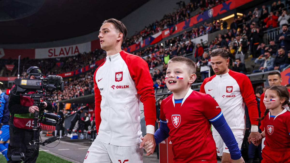 Dwaj chłopcy idący na boisko piłkarskie, jeden starszy w stroju reprezentacji Polski, drugi młodszy z pomalowaną twarzą.