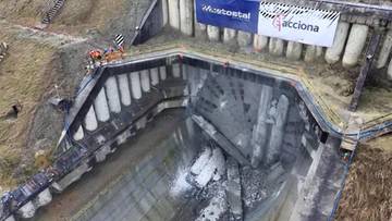 Widok z góry na budowę tunelu, z pracownikami na platformie i maszynami budowlanymi.