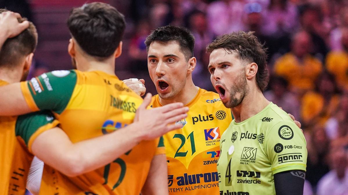 Trzech siatkarzy w akcji podczas meczu siatkówki. Dwóch z nich ma otwarte usta, wyrażając zaskoczenie lub emocje.