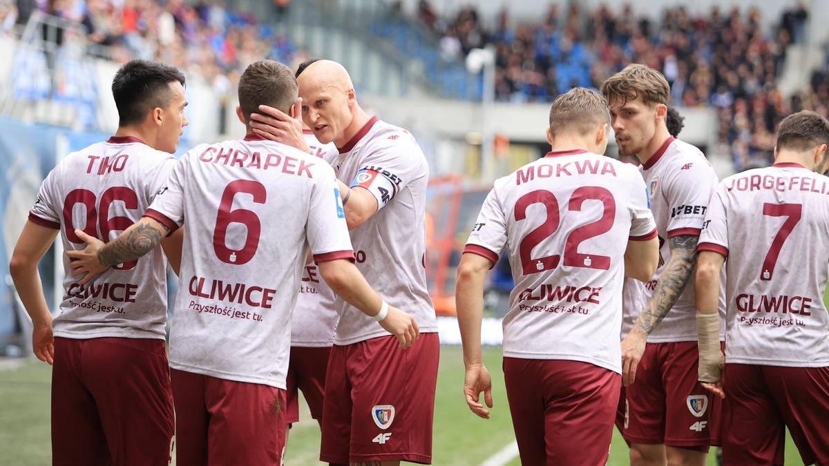 Grupa piłkarzy w bordowych strojach drużyny Piast Gliwice stojący blisko siebie na boisku.