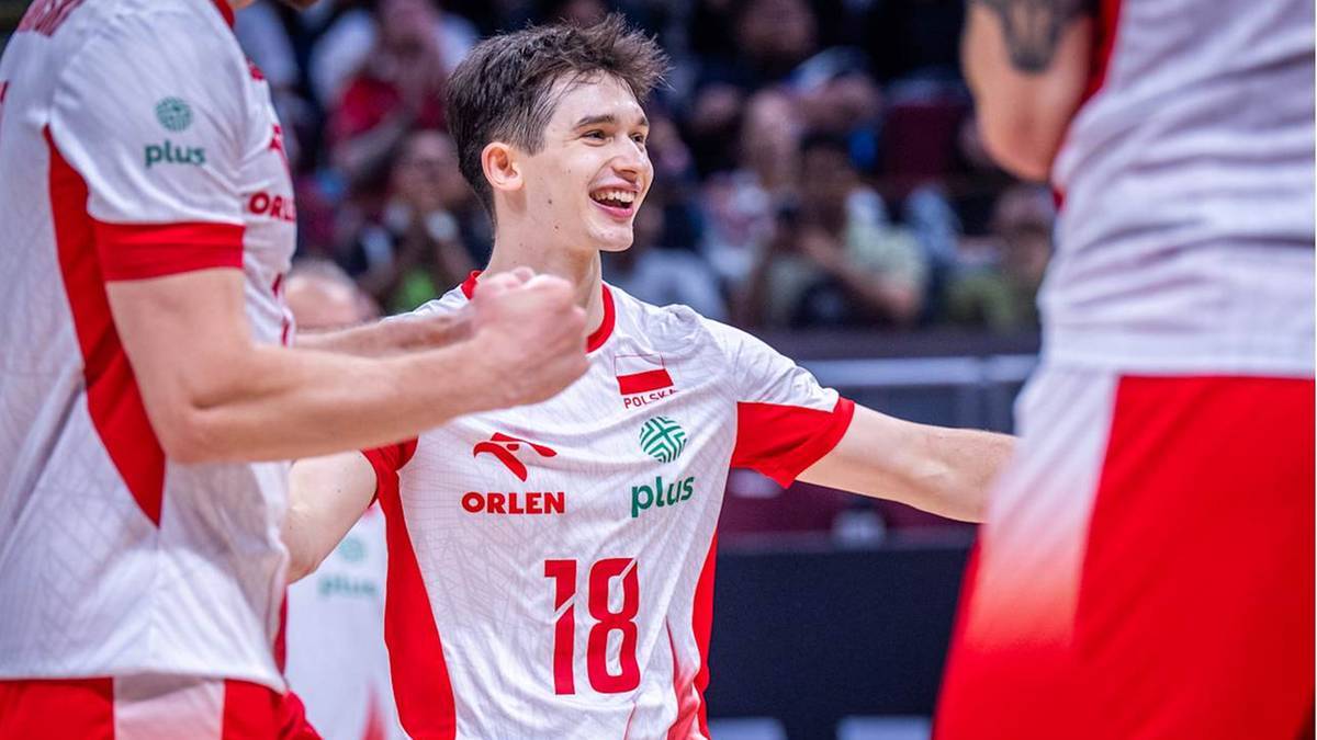 Uśmiechnięty siatkarz reprezentacji Polski w białej koszulce z czerwonymi rękawami i numerem 18, świętuje z kolegami z drużyny.