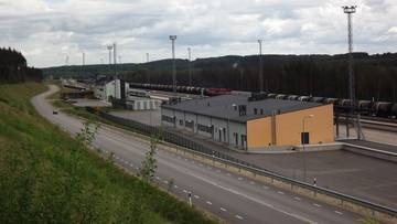 Widok na przejście graniczne z budynkami, drogami i torami kolejowymi w tle zalesionych wzg&oacute;rz.