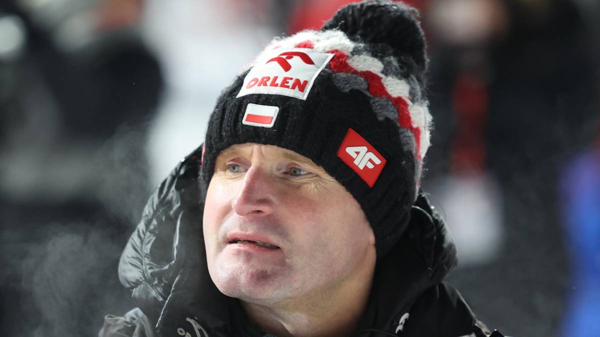 Portret mężczyzny w czapce zimowej z polskimi symbolami i logo, patrzącego w bok.