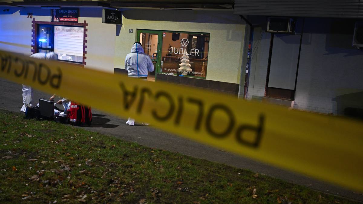 Policja zabezpiecza miejsce zdarzenia, taśma "POLICJA" na pierwszym planie, w tle funkcjonariusze w białych kombinezonach pracują przy wejściu do salonu jubilerskiego.