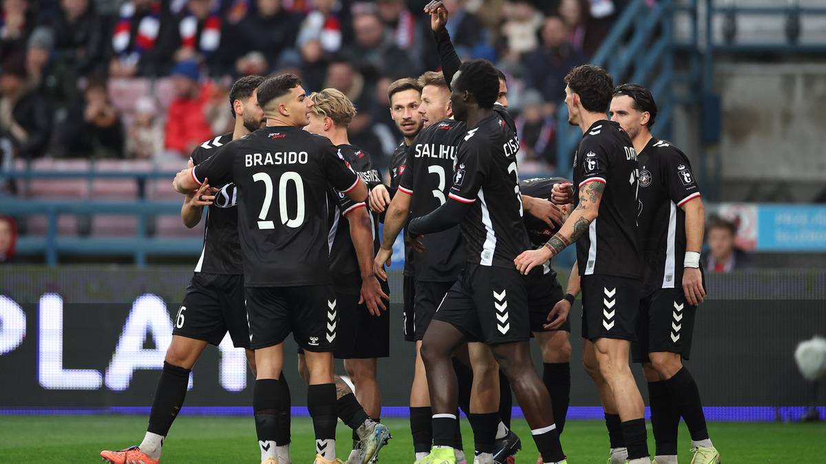 Drużyna piłkarzy w czarnych strojach świętuje na boisku.