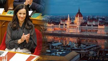 Uśmiechnięta kobieta klaszcząca przy biurku na tle nocnej panoramy Parlamentu w Budapeszcie nad Dunajem.