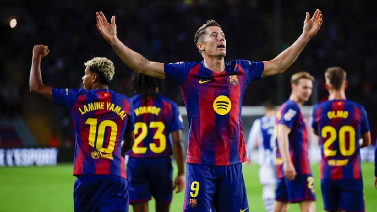 Piłkarze FC Barcelony w niebiesko-bordowych strojach świętują zwycięstwo na boisku. Robert Lewandowski, numer 9, unosi ręce w górę z wyrazem triumfu na twarzy. W tle widać innych zawodników z drużyny i kibiców.