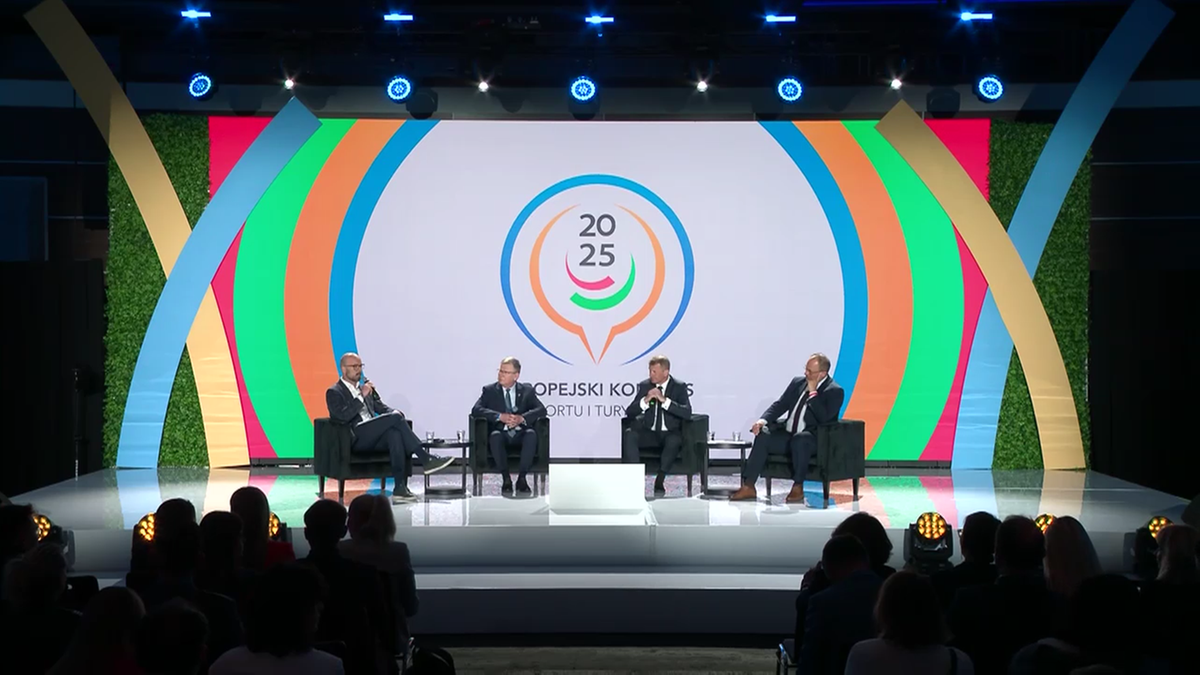 Czterech mężczyzn siedzi na scenie, podczas gdy trzeci panelista m&oacute;wi.