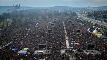 Widok z lotu ptaka na ogromny zgromadzenie ludzi w parku Letensk&eacute; sady w Pradze, z widocznymi scenami i panoramą miasta w tle.