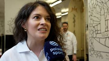 Kobieta z ciemnymi włosami, ubrana w białą koszulę, m&oacute;wi do mikrofonu z logo "Polsat Sport". W tle widać mężczyznę w białej koszuli.