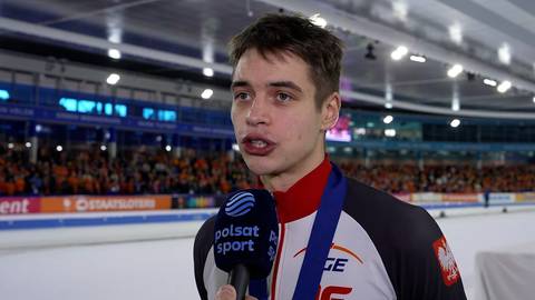 Młody mężczyzna w stroju sportowym z medalem na szyi udziela wywiadu, trzymając mikrofon.