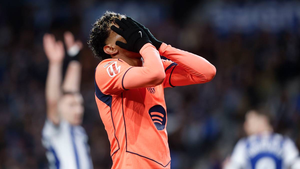 Piłkarz w pomarańczowej koszulce z czarnymi rękawiczkami zakrywa twarz dłońmi, wyrażając frustrację.