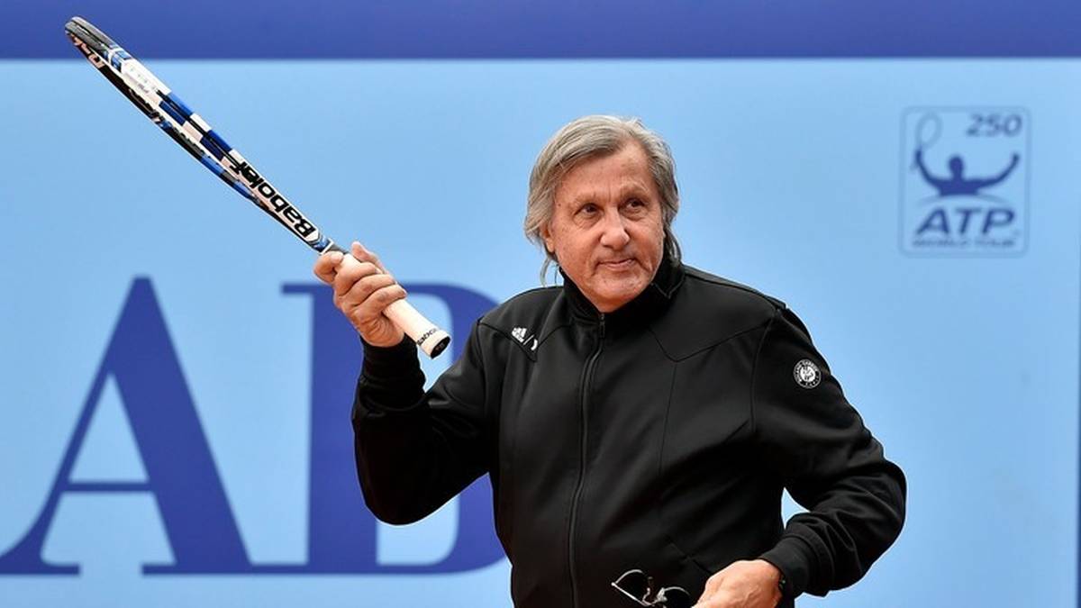 Ilie Nastase, były tenisista, trzyma rakietę tenisową nad głową.