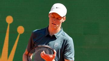 Tenisista Jannik Sinner trzyma rakietę w ręku na tle logo Rolex.