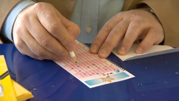 Dłoń mężczyzny trzymająca ołówek i zaznaczająca liczby na kuponie lotto.