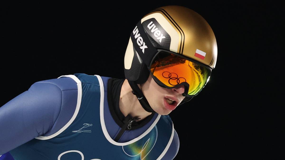 Skoczek narciarski w kasku i goglach na ciemnym tle.