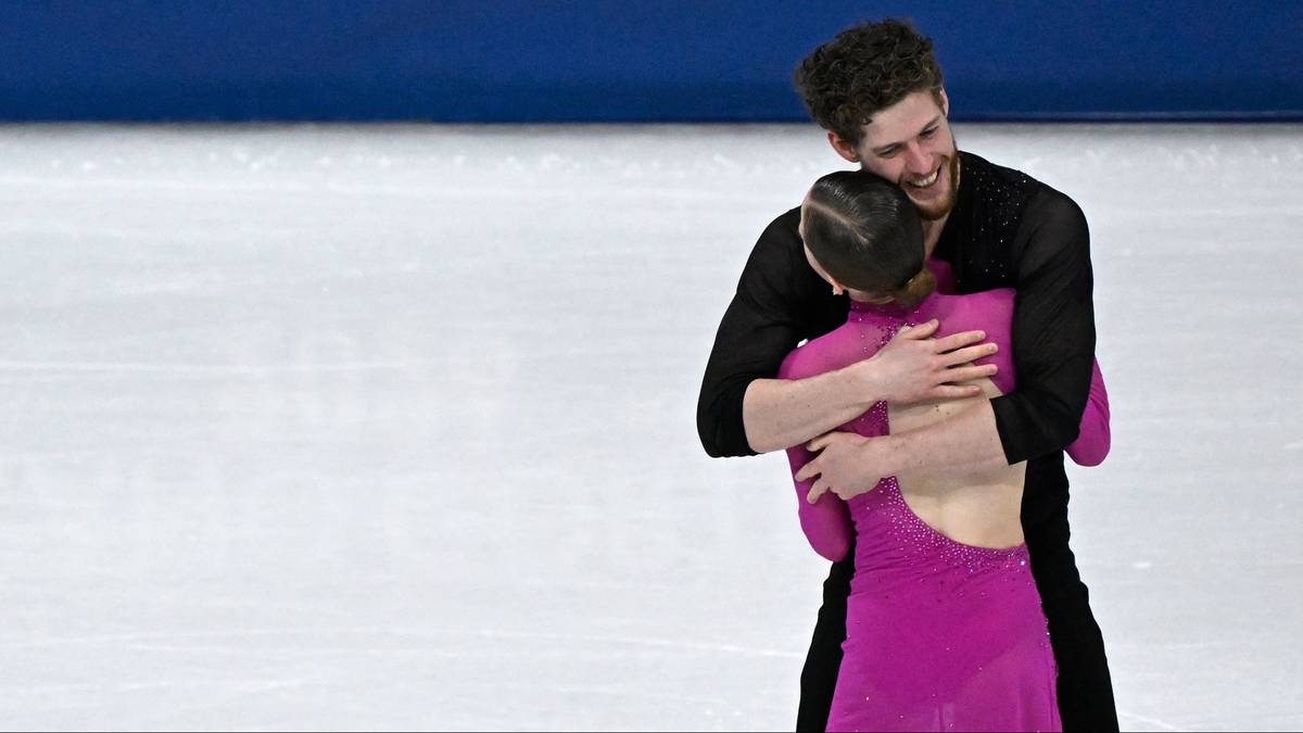 Para łyżwiarzy figurowych obejmuje się na lodowisku, na tle niebieskiego banera z napisem "MILANO CORTINA 2026".