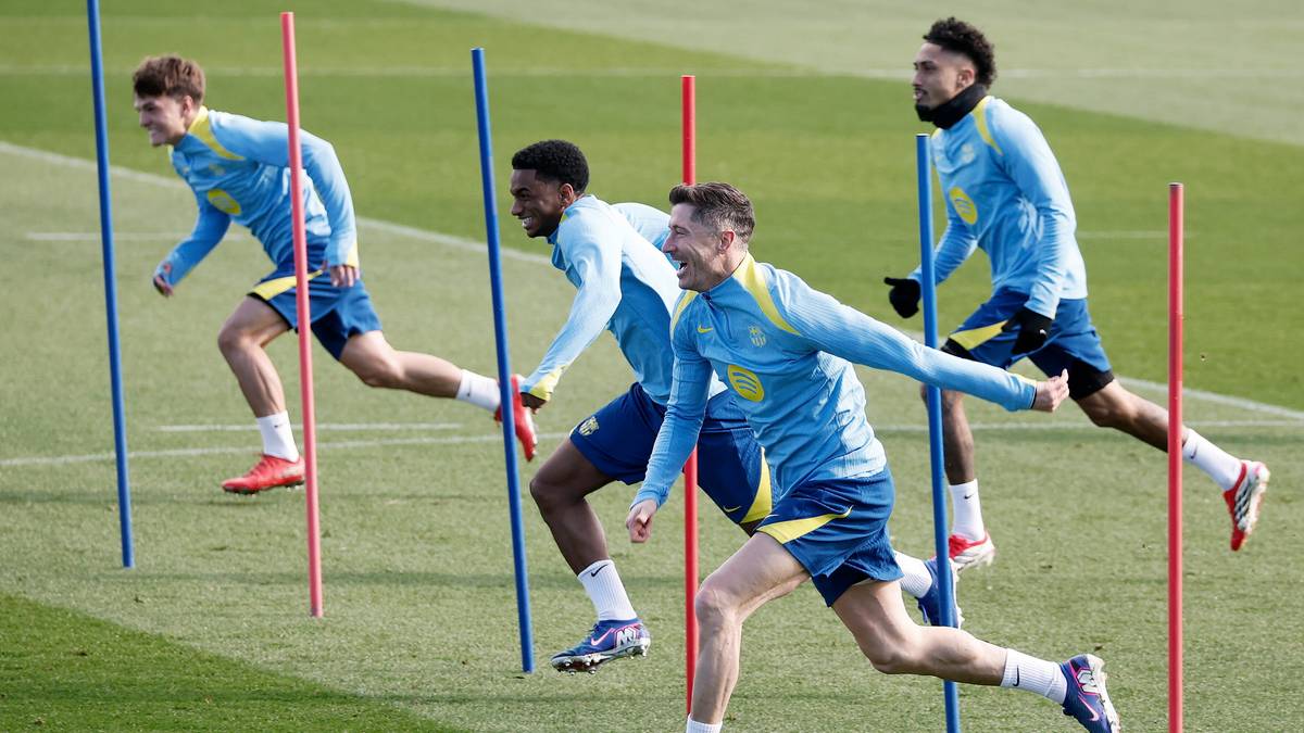 Piłkarze FC Barcelony wykonujący ćwiczenia z tyczkami na boisku treningowym.