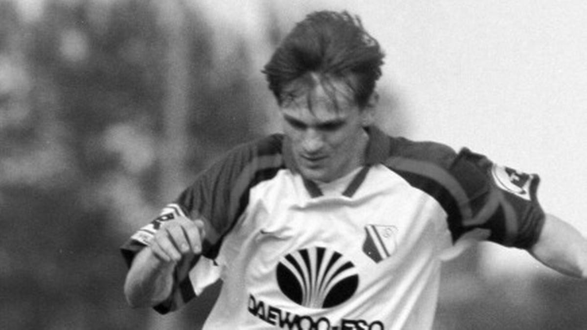 Dw&oacute;ch piłkarzy grających w piłkę nożną, jeden w białej koszulce pr&oacute;buje odebrać piłkę przeciwnikowi.