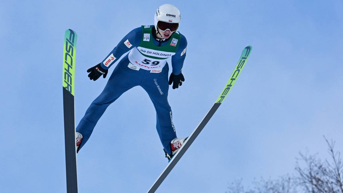 Skoczek narciarski w powietrzu na tle błękitnego nieba.