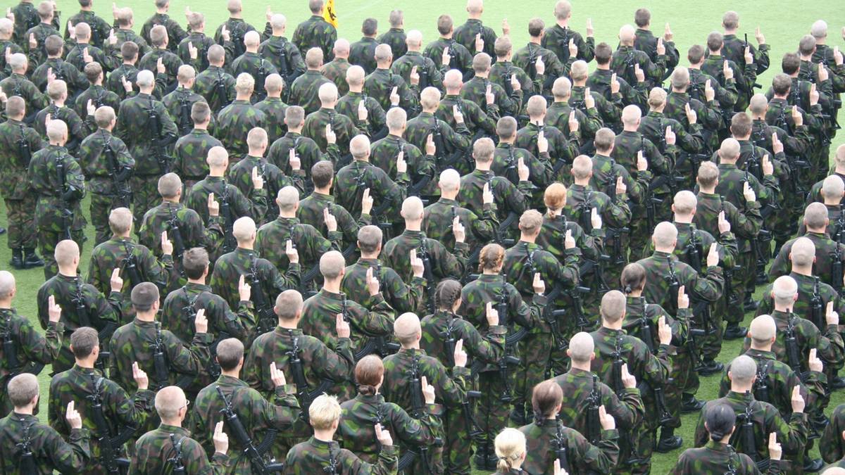 Duża grupa żołnierzy w ciemnozielonych mundurach stojąca w formacji na trawie.
