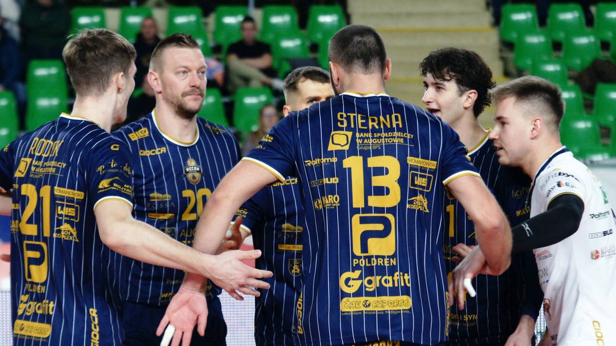 Siatkarze w granatowych strojach sportowych z ż&oacute;łtymi pasami rozmawiają między sobą na boisku siatkarskim.