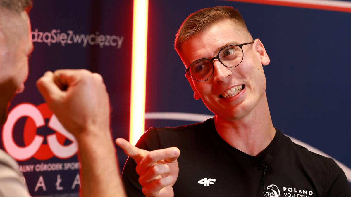 Mężczyzna w okularach i czarnej koszulce z napisem "POLAND VOLLEYBALL" wskazuje palcem w stronę rozm&oacute;wcy.