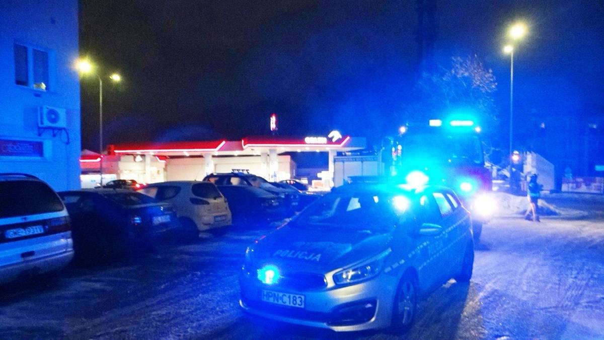 Samochody policyjne z włączonymi niebieskimi sygnałami świetlnymi na tle nocnego, oświetlonego ulicznymi latarniami miejsca.