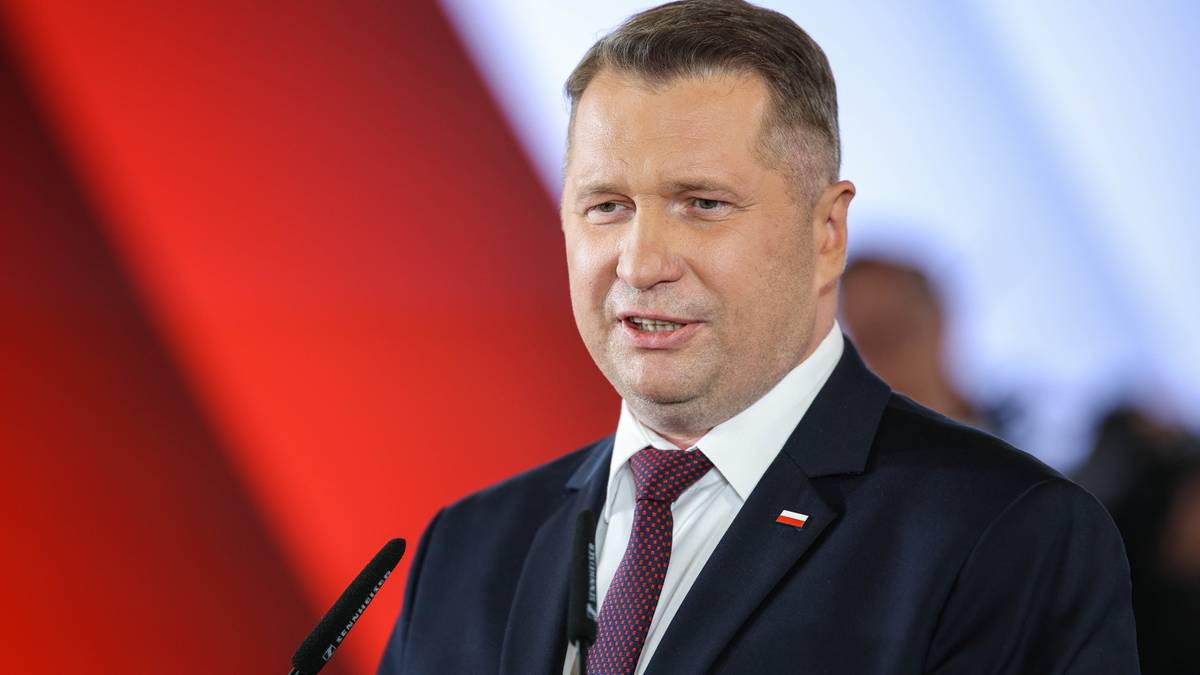 Przemysław Czarnek w garniturze i krawacie przemawia za m&oacute;wnicą.