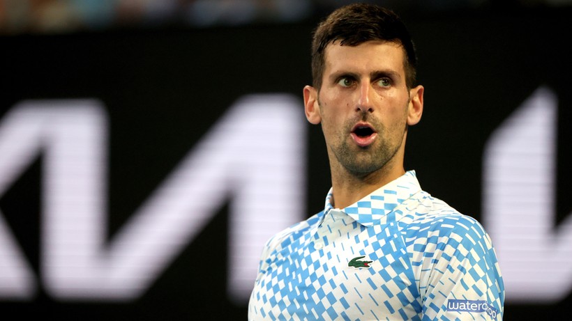 Novak Djoković w białej koszulce polo z niebieskimi wzorami na tle ciemnego ekranu z białym logo.