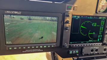 Widok z kokpitu śmigłowca z ekranem kamery termowizyjnej pokazującym sylwetkę człowieka na polu.
