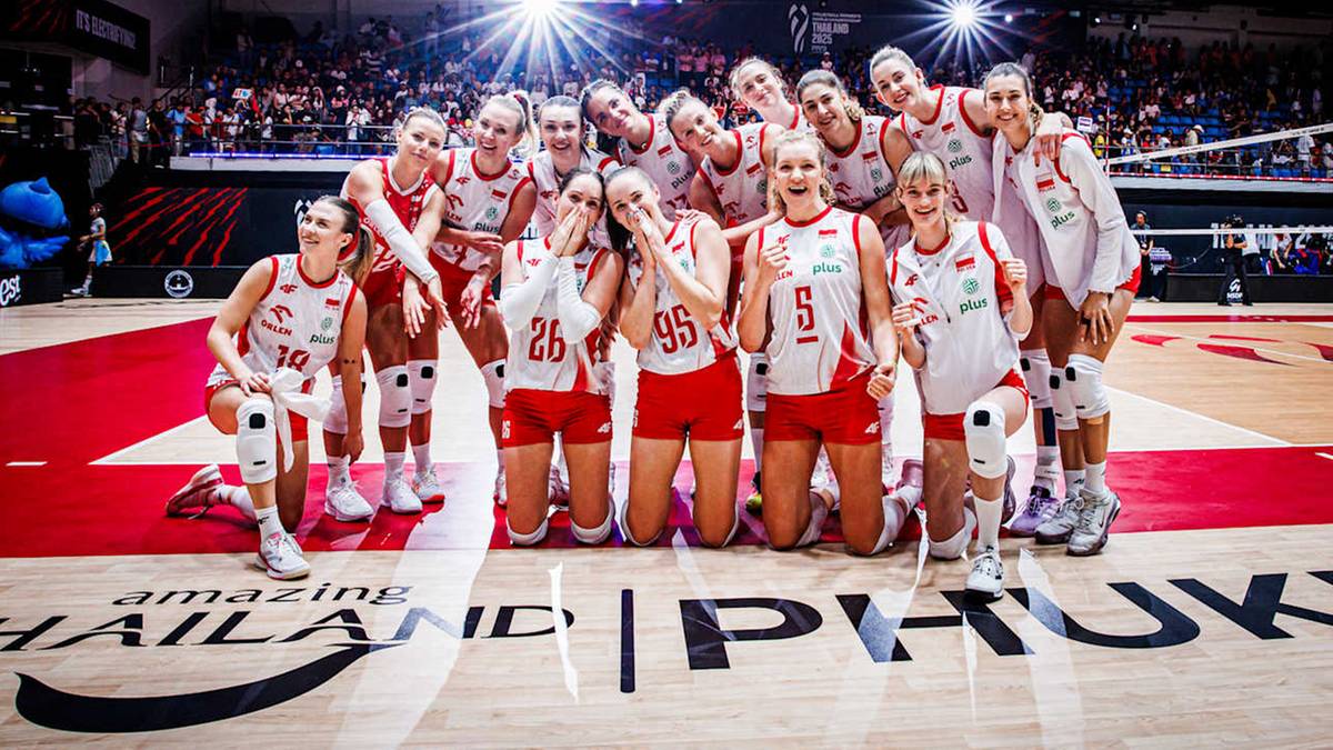 Grupa zawodniczek siatkówki w białych strojach z czerwonymi akcentami, pozujących do zdjęcia na boisku.