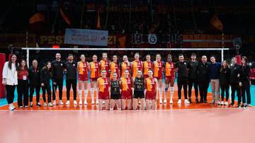 Dwie drużyny siatkarskie pozujące do zdjęcia na boisku przed meczem, z publicznością na trybunach w tle.