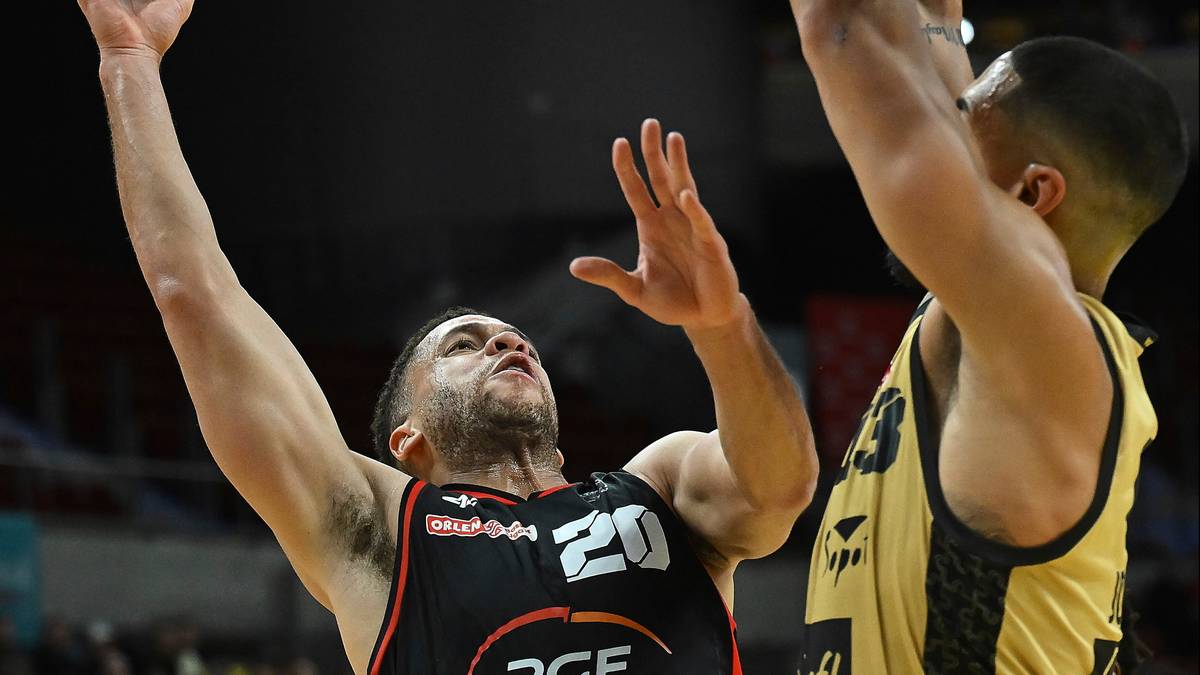 Gracz w koszykówkę w czarnej koszulce z numerem 20 próbuje rzucić piłkę, podczas gdy inny zawodnik w żółtej koszulce blokuje jego zagranie.