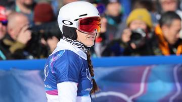 Snowboardzistka w białym kasku i goglach narciarskich z czerwonymi szkłami, ubrana w str&oacute;j sportowy, patrzy w bok.