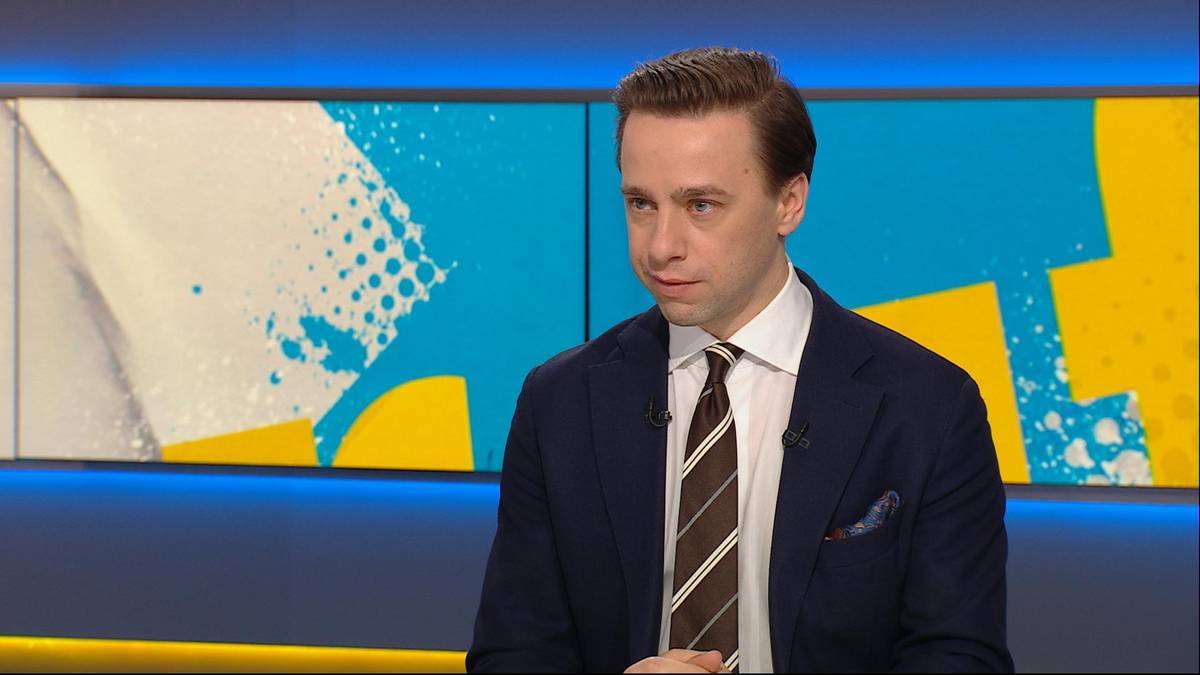 Krzysztof Bosak w garniturze i krawacie siedzi przed ekranem z abstrakcyjnym wzorem.