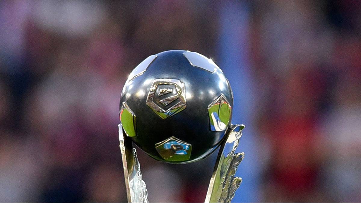 Czarna piłka nożna z ozdobnymi, lustrzanymi panelami umieszczona na złotym trofeum, z rozmytym tłem stadionu.