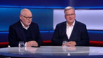 Dw&oacute;ch starszych mężczyzn w garniturach siedzi naprzeciwko siebie przy stole. Przed każdym stoi szklanka wody.