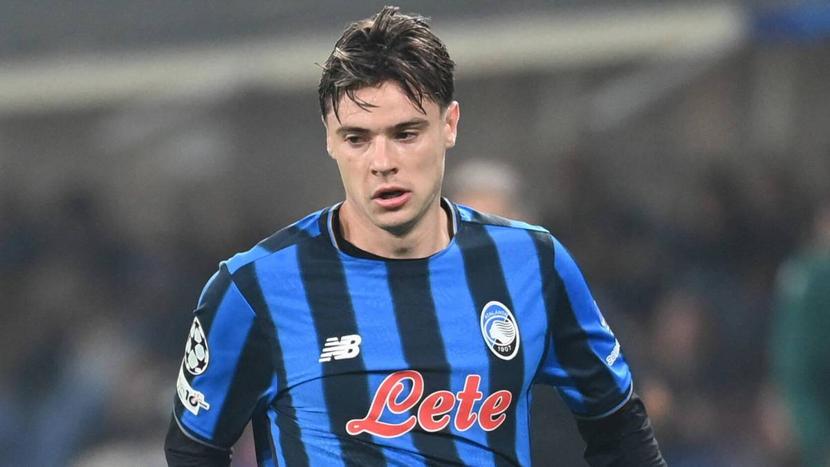 Młody mężczyzna w niebiesko-czarnej koszulce piłkarskiej z logo Loto i herbem klubu, na tle stadionu.