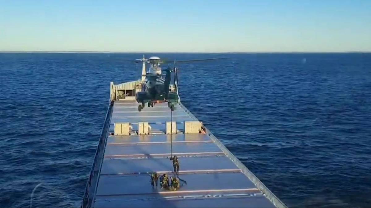 Śmigłowiec transportowy opuszczany na pokład statku towarowego na pełnym morzu.