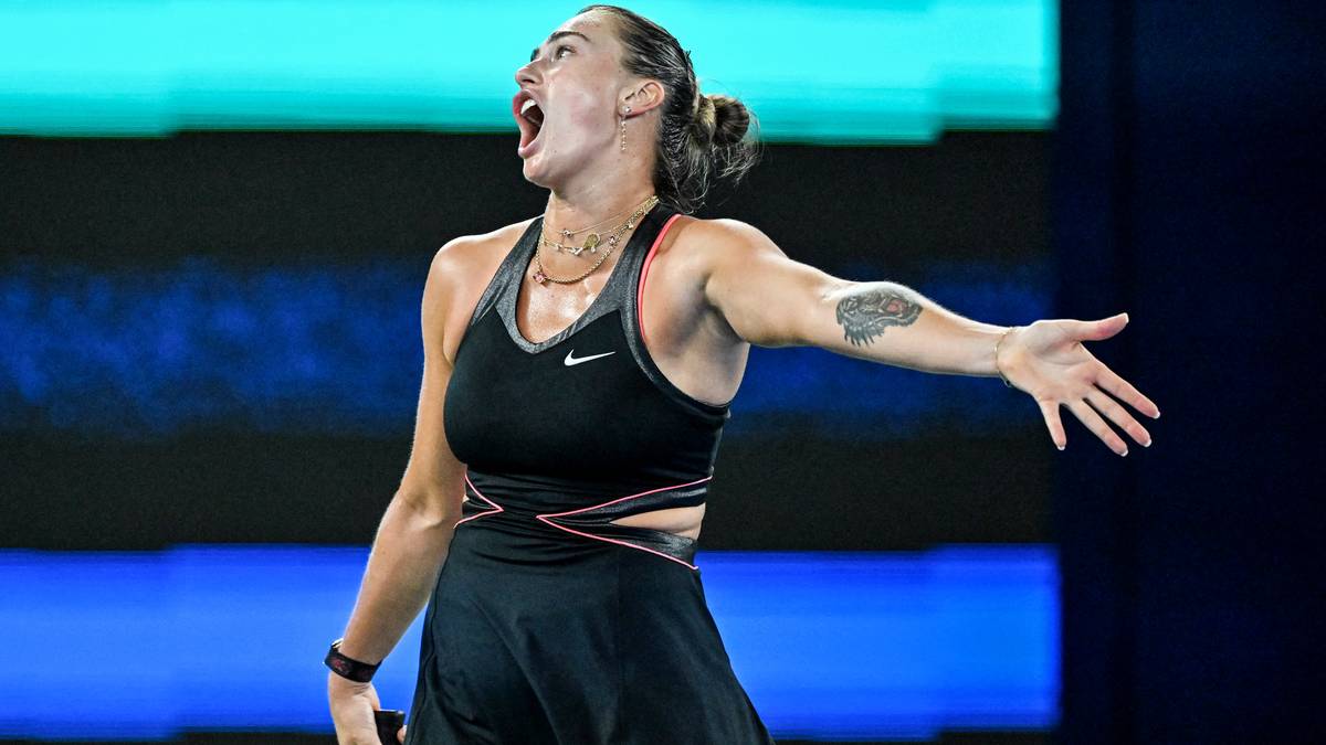 Aryna Sabalenka podczas meczu tenisowego, z otwartymi ustami i uniesionymi ramionami, wyrażająca silne emocje.